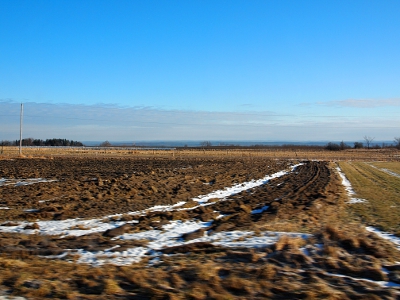 [Plowed dirt with streaks of snow in the parts of it. Clear blue skies above a swath of clouds across the horizon.]